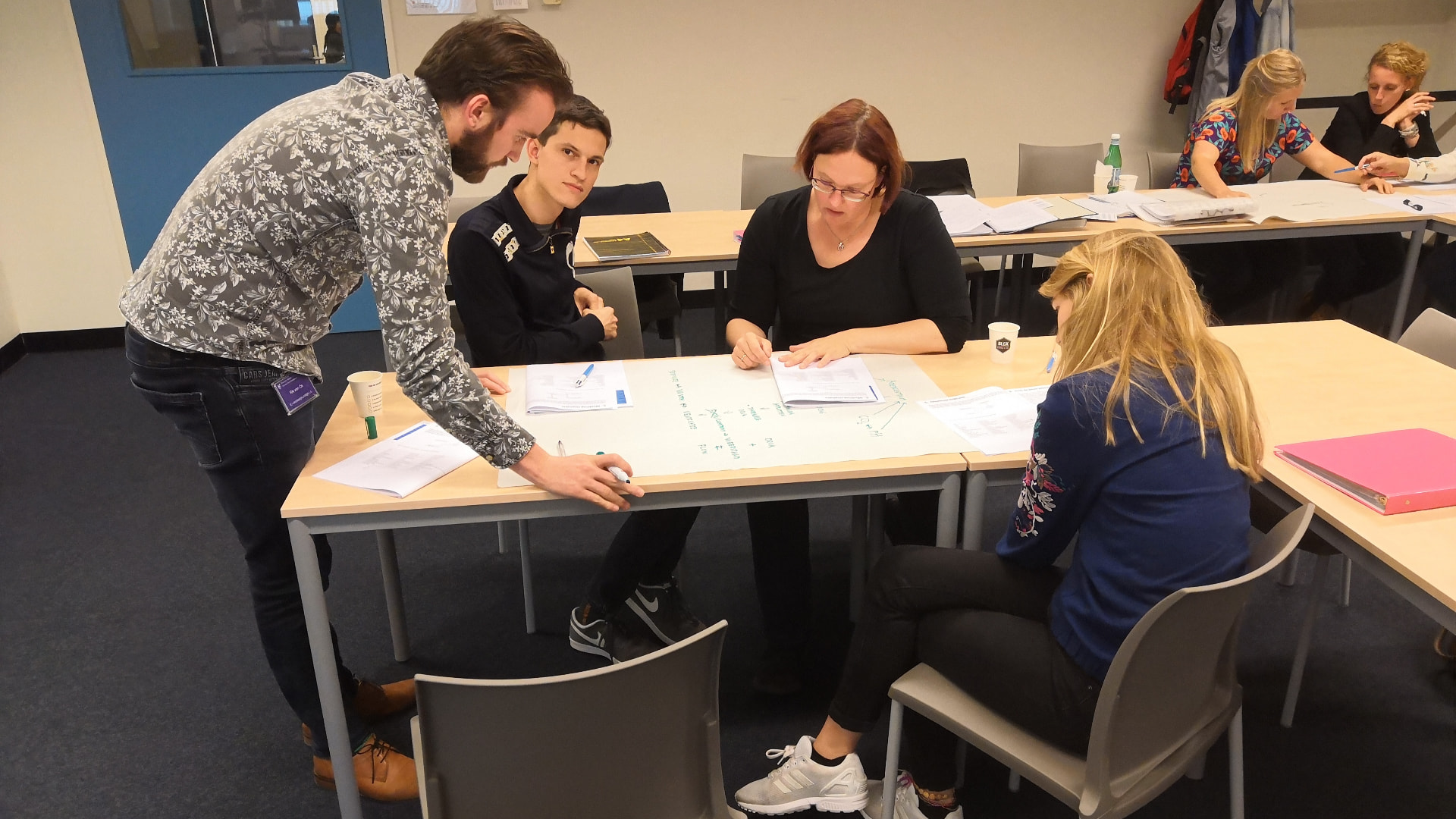 Docent begeleidt een groepje studenten dat samen een casus uitwerkt op papier.