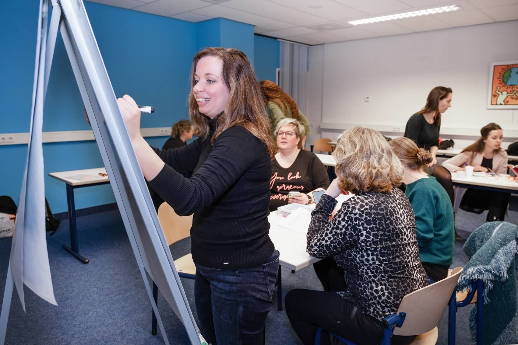 Docent schrijft op een flipover terwijl studenten in het lokaal meedenken.