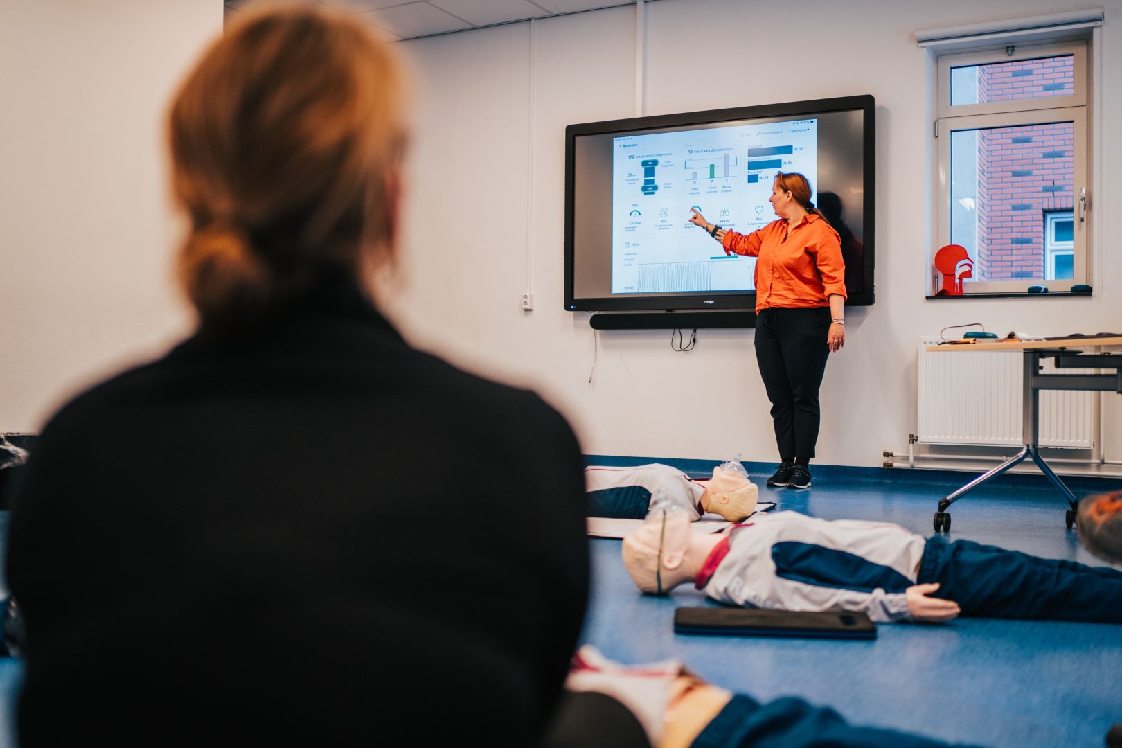 Docent bespreekt reanimatiefeedback op een scherm tijdens een training met reanimatiepoppen.