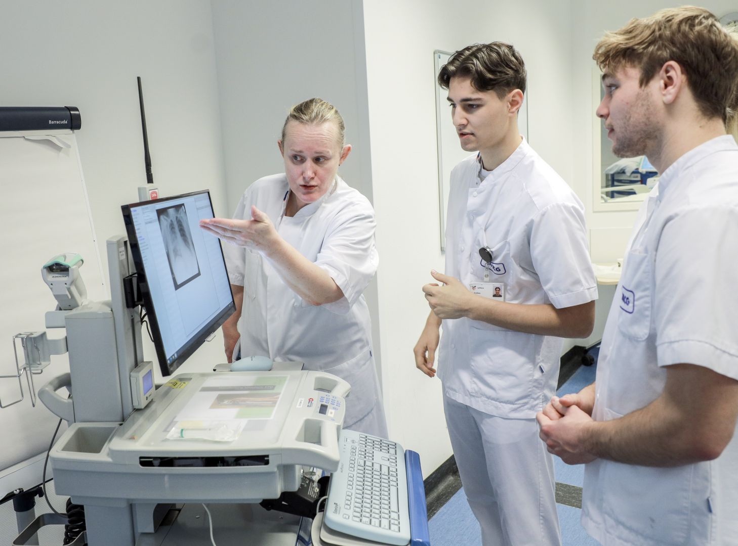 Zorgprofessional bespreekt een röntgenbeeld op een monitor met twee studenten op de afdeling.